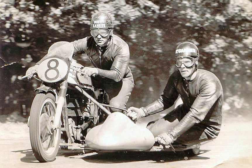 Two men on a 1950's motorbike and sidecar.  The photo is black and white
