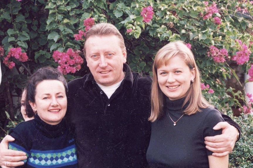 Kerry Salinger (left) with Gennadi Bernovski and his wife Svetlana stand in front of purple flowers on a vine.
