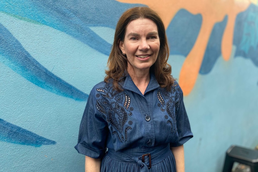 Suzie Holt smiles at the camera while standing in front of a mural.