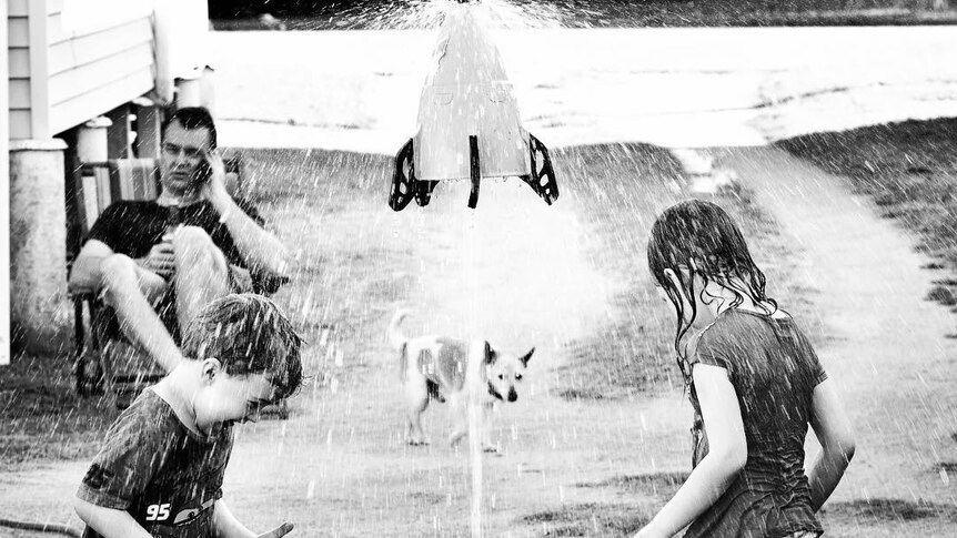 Children and their dog play under a sprinkler.