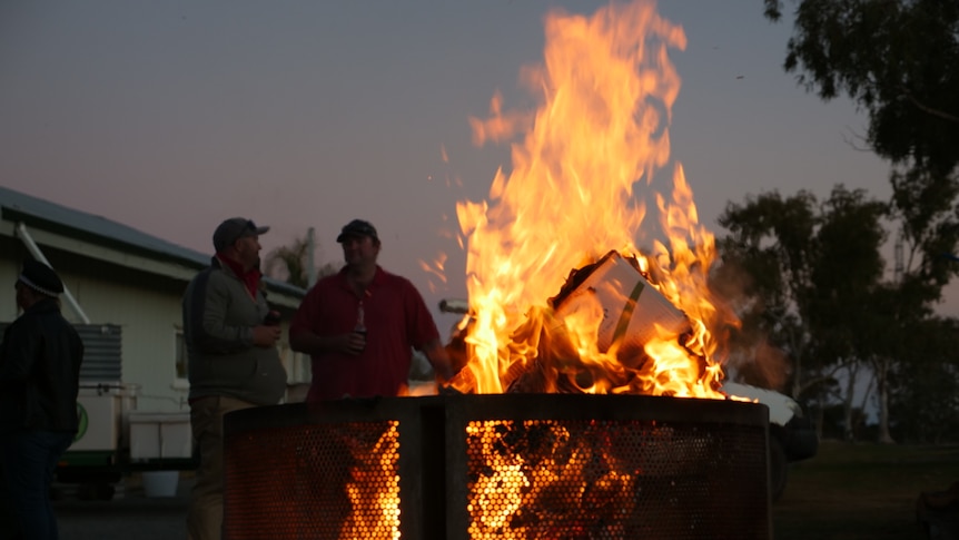 picture of two men talking to each other by a fire.