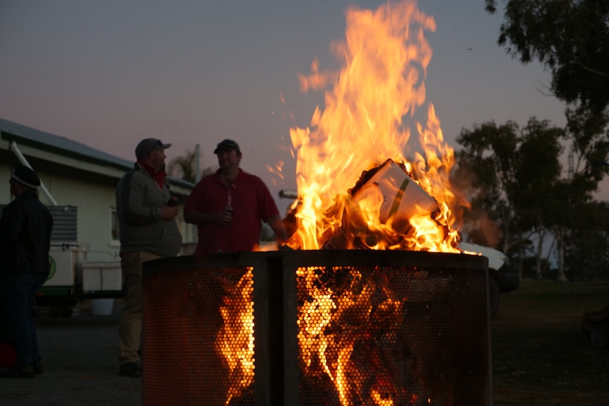 picture of two men talking to each other by a fire.