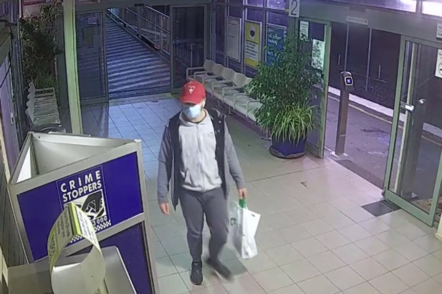 A man wearing a red cap walks through a train station holding a shopping bag.