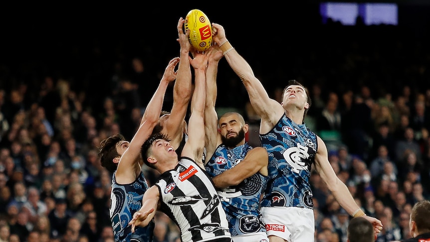 Collingwood and Carlton players jump and reach for an AFL ball during a game.