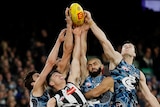 Collingwood and Carlton players jump and reach for an AFL ball during a game.
