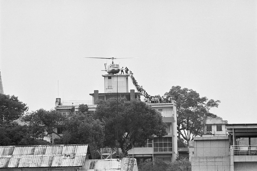 A black and white photo shows people filing up a set of stairs and onto a helicopter on top of a building