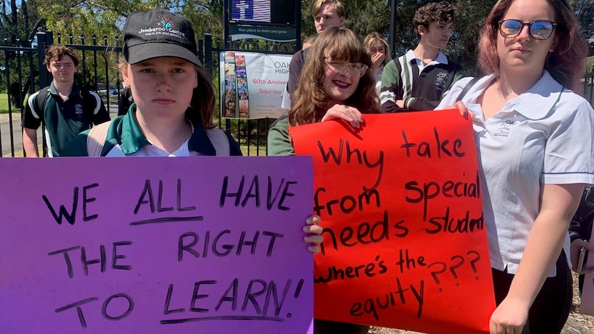 Three teenage girls in school uniform holding protest signs