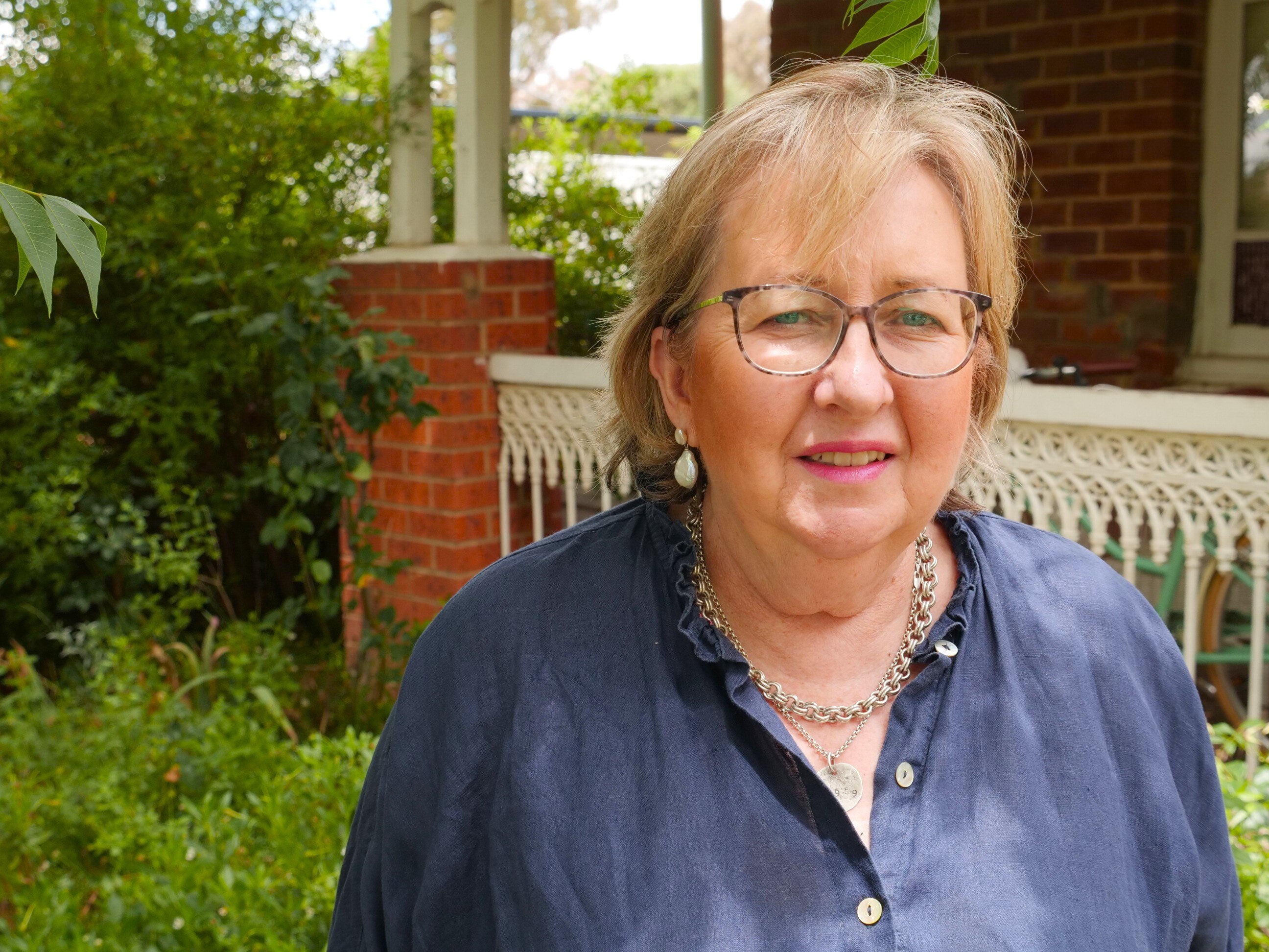 A woman looking concerned, standing outside a house.