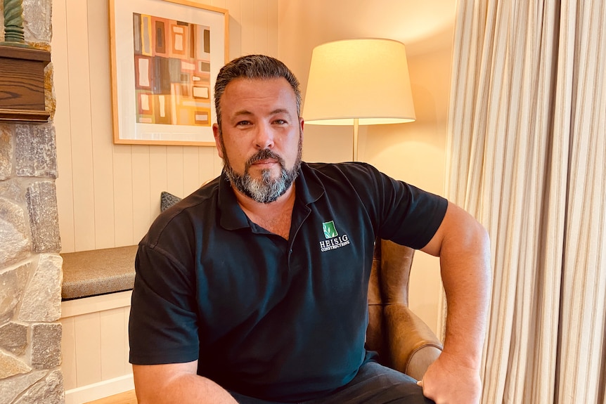 a man sits in a brown armchair looking directly at the camera wearing a business branded polo shirt