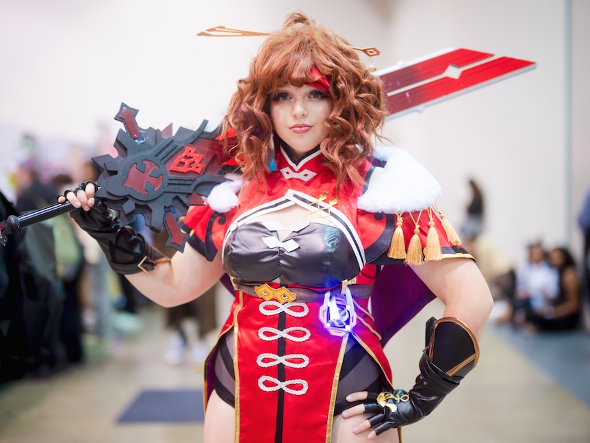 A woman dressed in a cosplay outfit, holding a sword and wearing doll-like make-up.