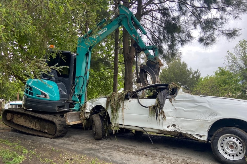 Squashed white ute picked up by machinery