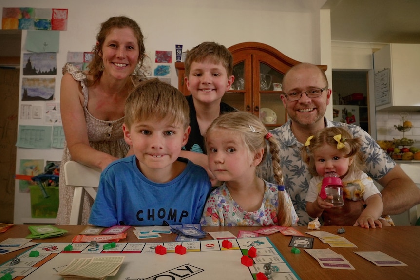 Une famille avec quatre enfants regarde directement la caméra avec un panneau de monopole sur la table devant