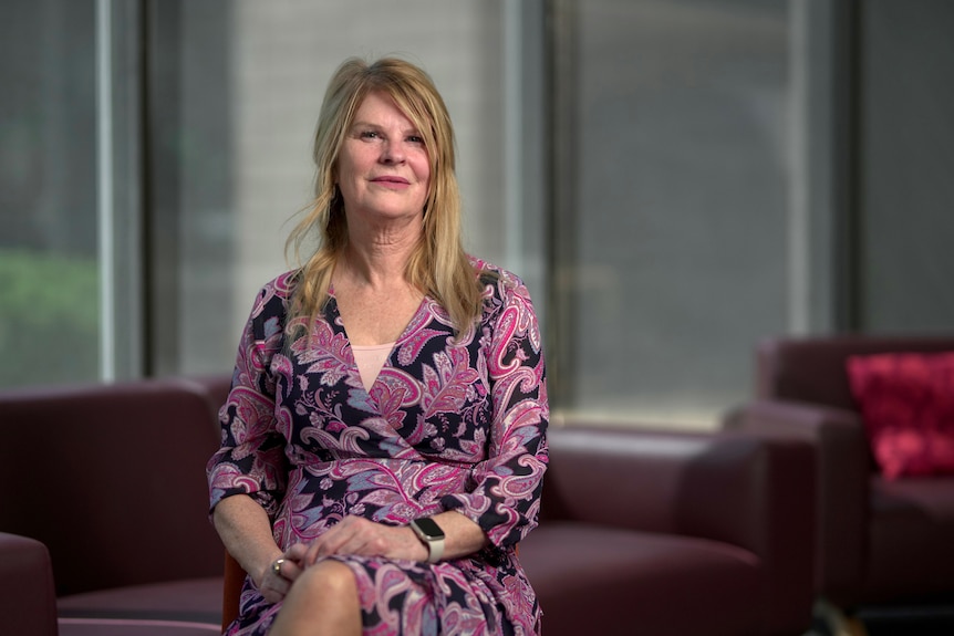 A blonde woman in a pink dress sitting on a maroon couch