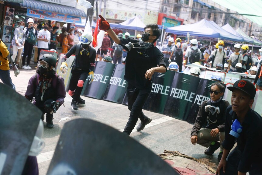 Les manifestants portant des masques à gaz utilisent des boucliers de fortune avec "gens" écrit sur le devant pour former une ligne défensive.