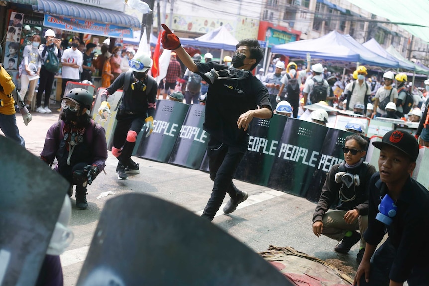 Protesters wearing gas masks use makeshift shields with "people" written on the front to form a defensive line.