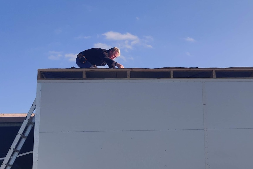 A man on a tiny house roof 