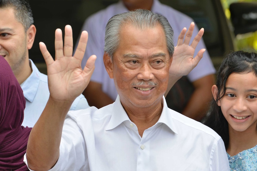 Politician Muhyiddin Yassin waves to media wearing a white shirt.