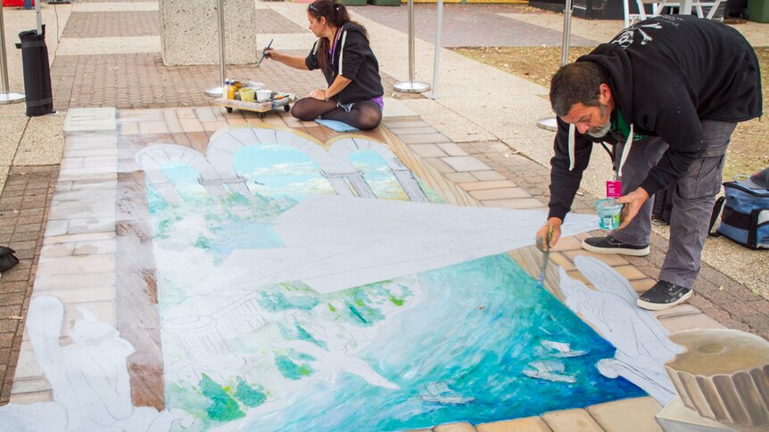 Artist Amelia Batchelor and Dom Intelisano paint on the pavement for the 3D chalk art installation.