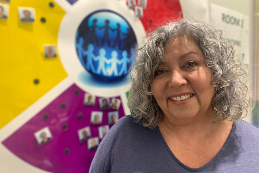 A woman with curly hair standing in front of colourful work sign smiling