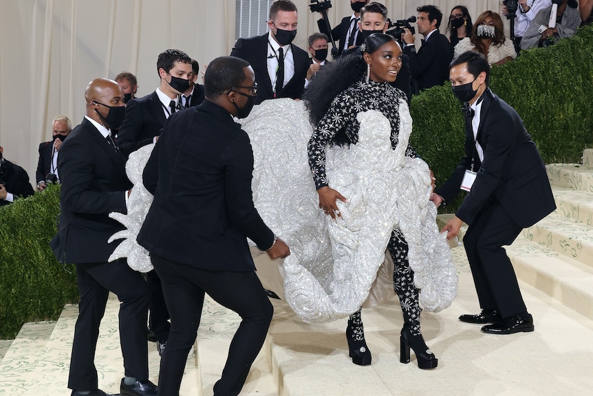 Woman gearing a gown with a group of men carrying the train at an event