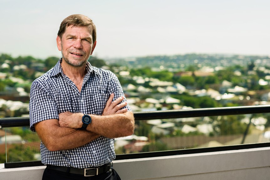 Graham Turner, director ejecutivo de Flight Center Travel Group, con los brazos cruzados en un balcón con casas entre árboles detrás de él