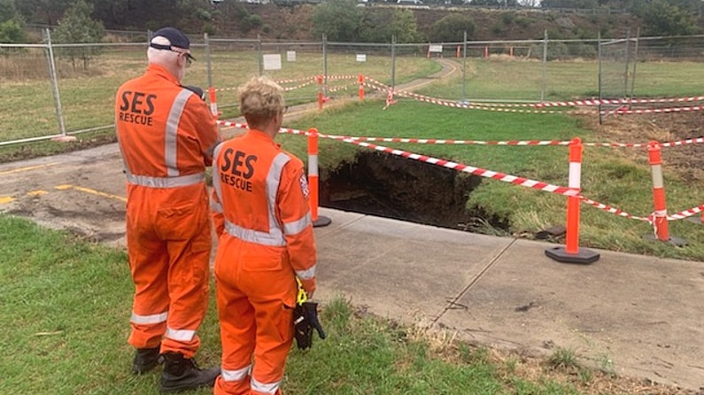 Two SES workers in orange jumpsuits stand near a sinkhole that is fenced off.