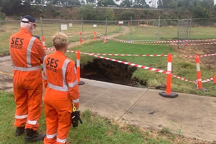 Two SES workers in orange jumpsuits stand near a sinkhole that is fenced off.