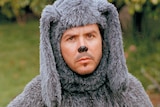 A man dressed like a dog with a painted black nose and a grey fluffy dog suit.