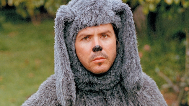 A man dressed like a dog with a painted black nose and a grey fluffy dog suit.