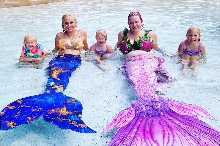 Two mermaids in water with three children