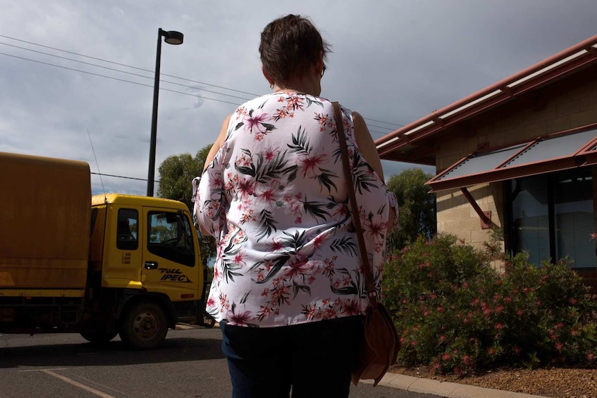 A woman with a flowery top stands with her back to the camera in a car park.