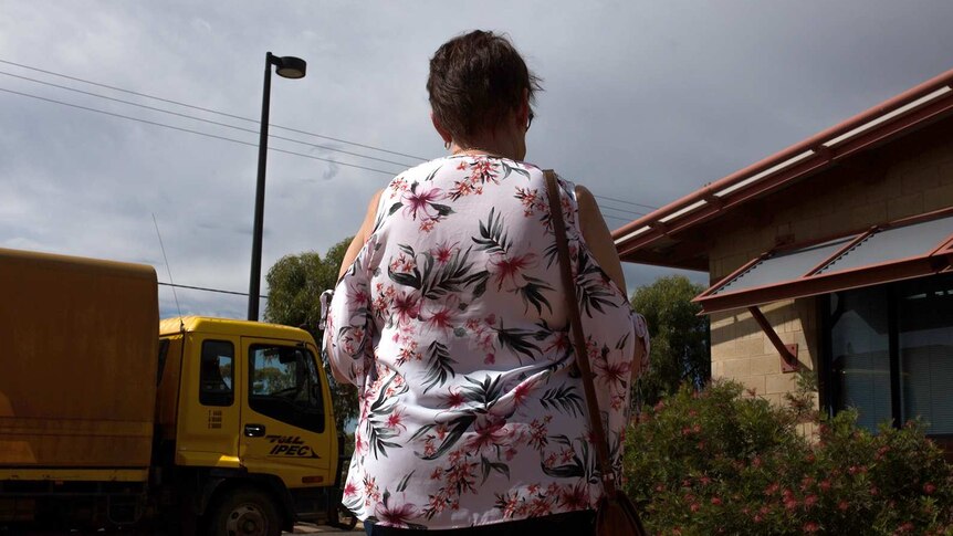 A woman with a flowery top stands with her back to the camera in a car park.