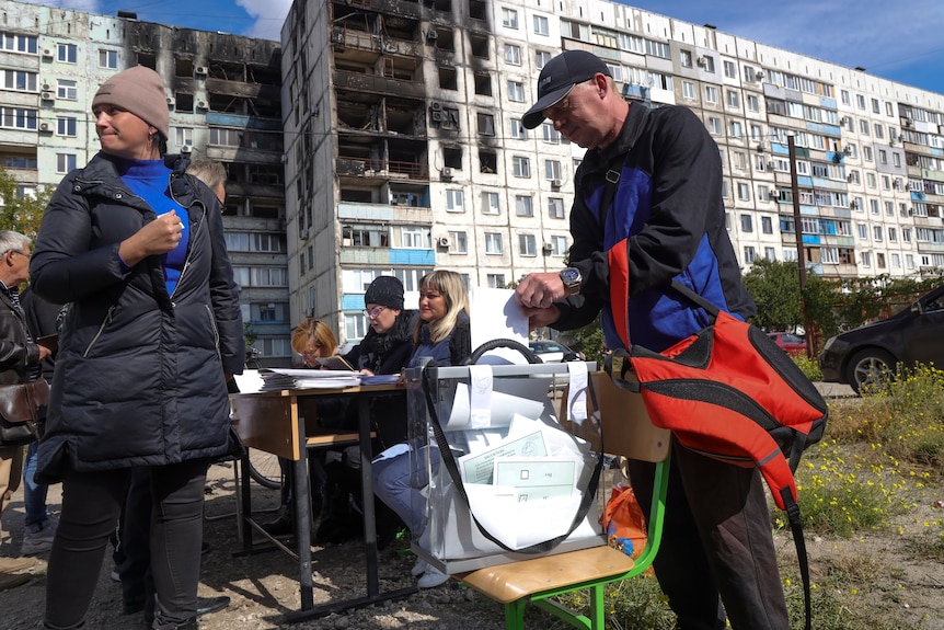 People vote at mobile polling station outside destroyed apartment building. 