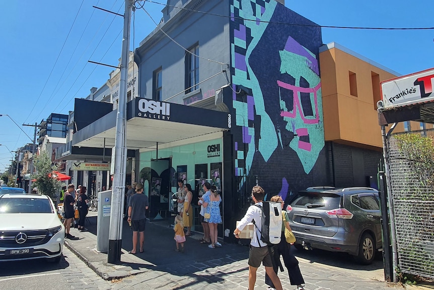 The brightly painted exterior of a brick building with people standing around on the footpath outside.