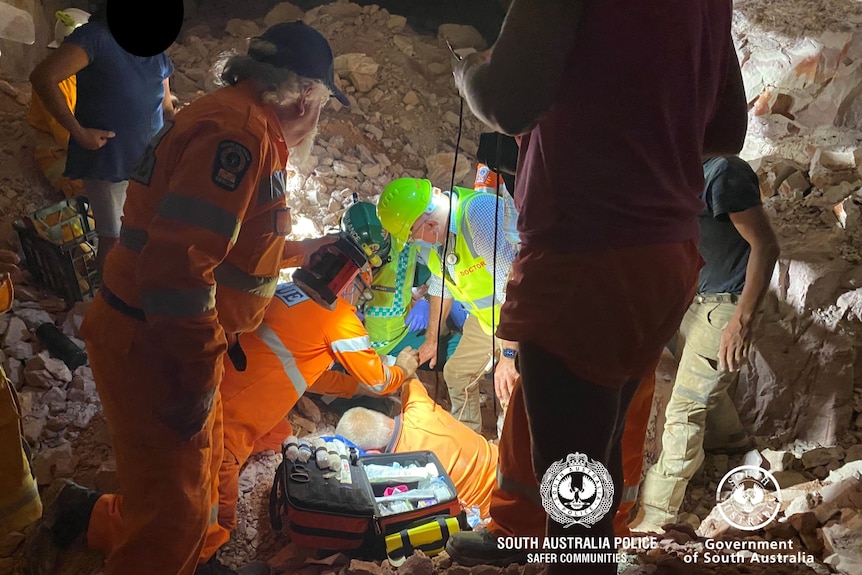 Emergency service workers crowd around a hole as a miner is winched to safety