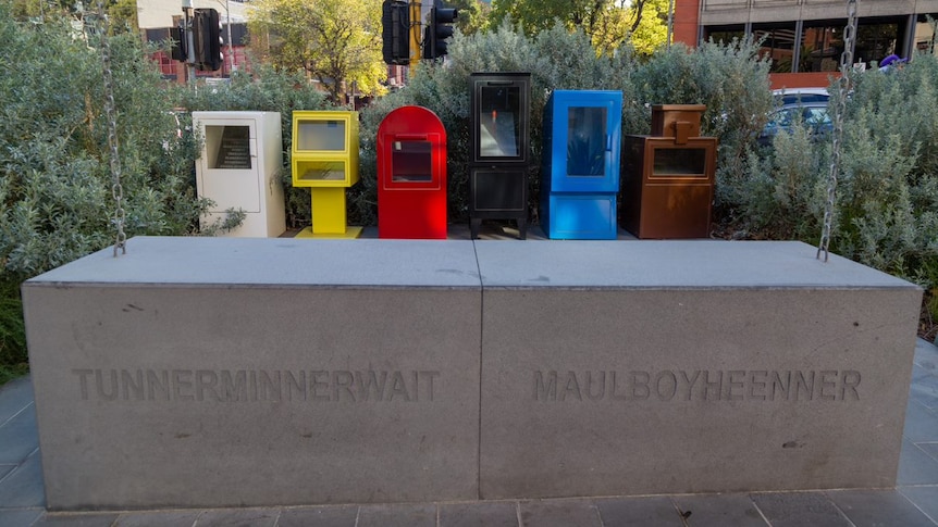 Colourful news stands sit behind concrete memorial blocks engraved with the names Tunnerminnerwait and Maulboyheenner.