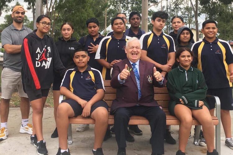 A group of mainly pacific Islander youth with an older white male giving a thumbs up, in a park