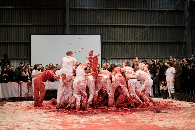 A group of people fight over a bull carcass watched by an audience.