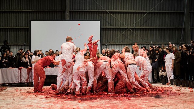 A group of people fight over a bull carcase watched by an audience.
