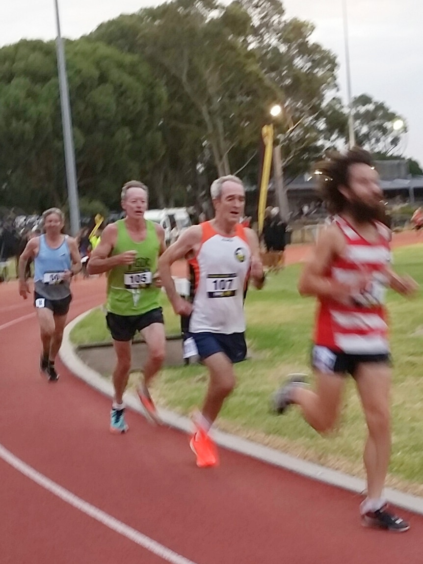 quatre hommes qui courent sur une piste de course rouge.