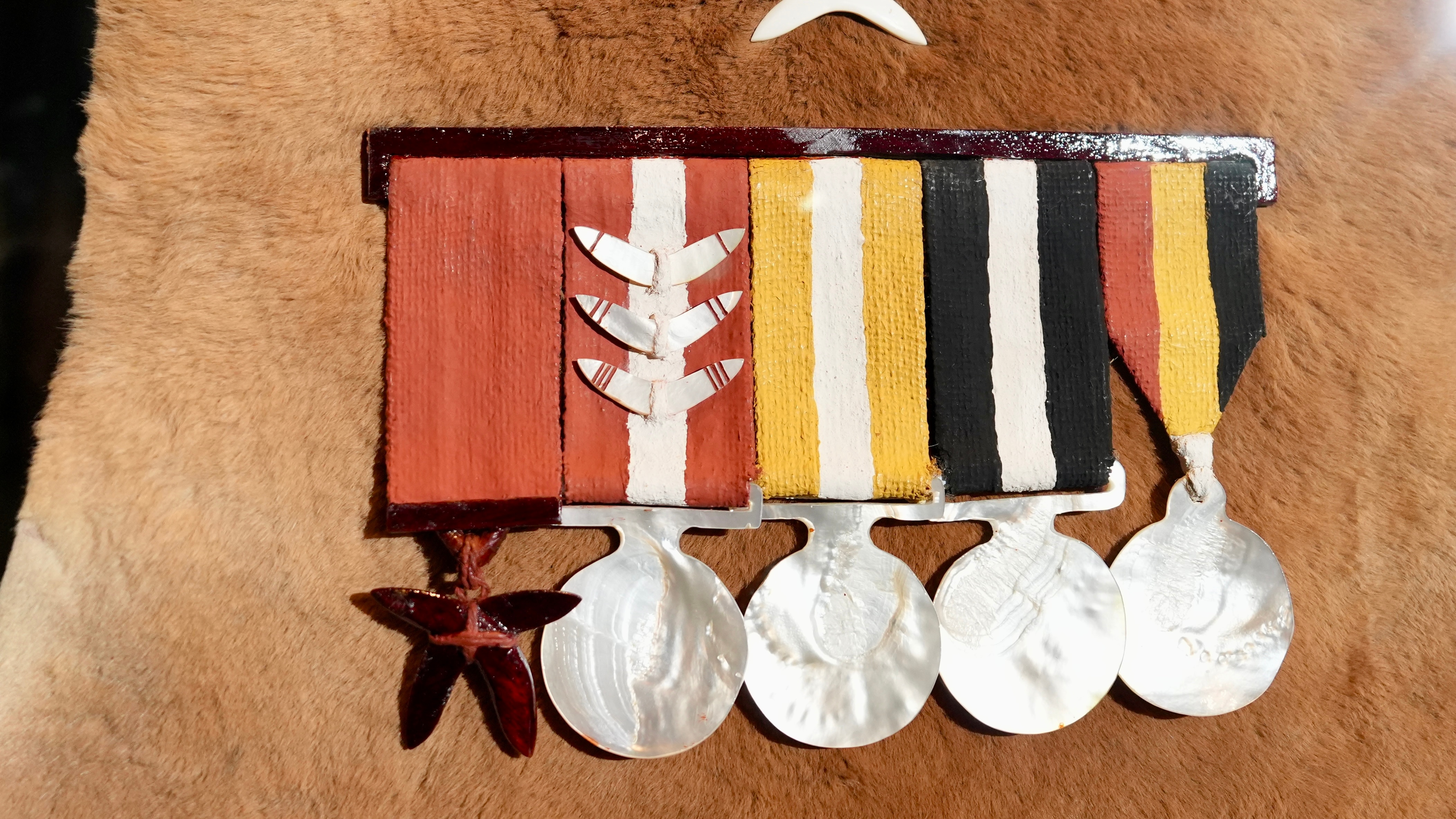 A close-up view of a kangaroo hide with First Nations-style artistic representation of Australian war medals pinned to it.