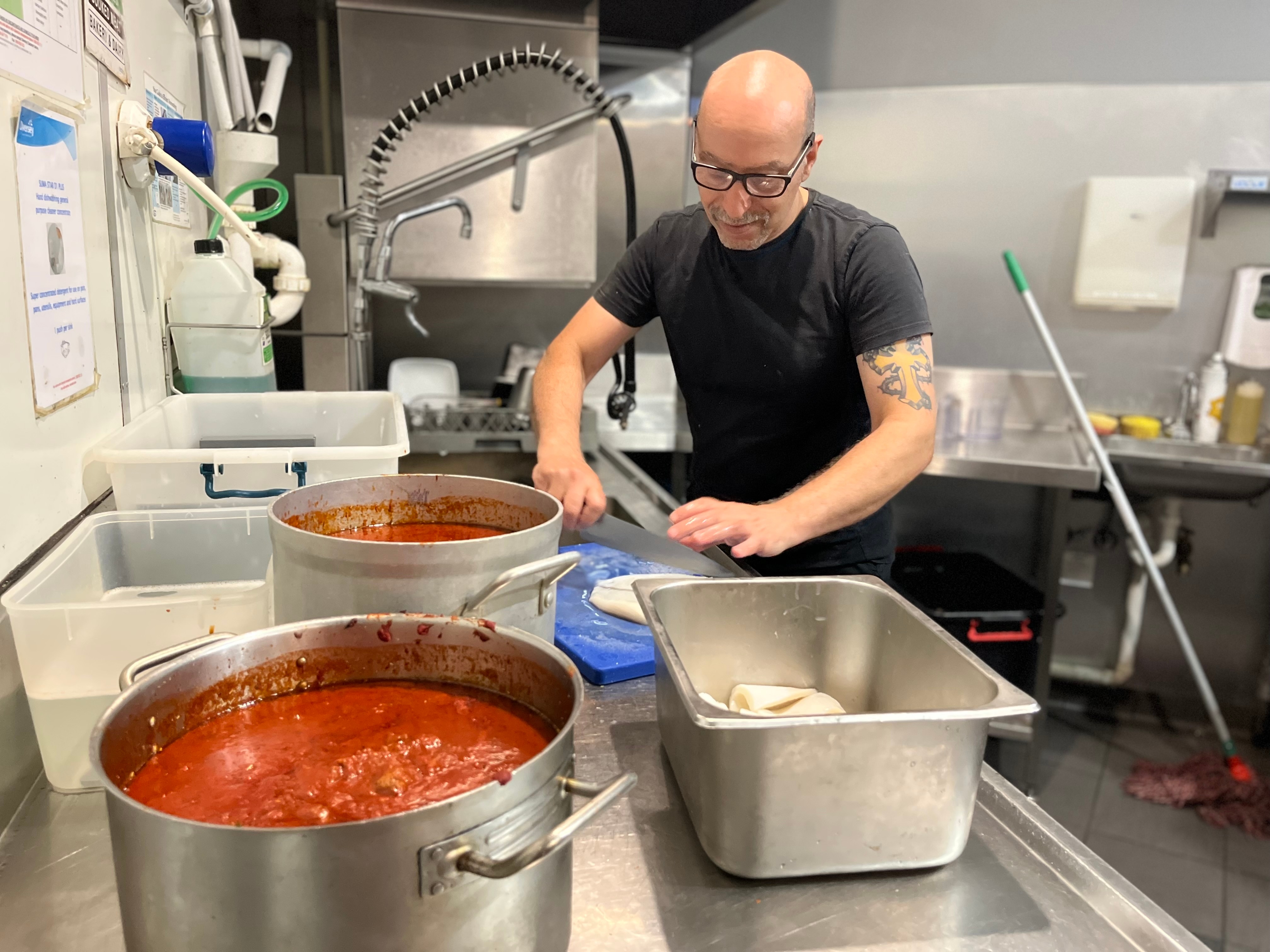 A man cuts up a white fish in an industrial kitchen. 