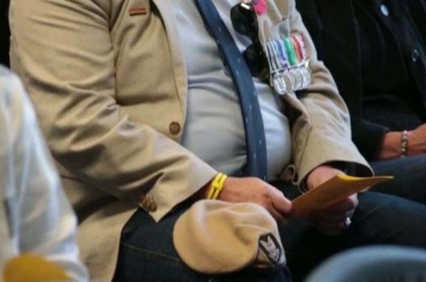 Torso of a man sitting wearing war medals and holding a pamphlet