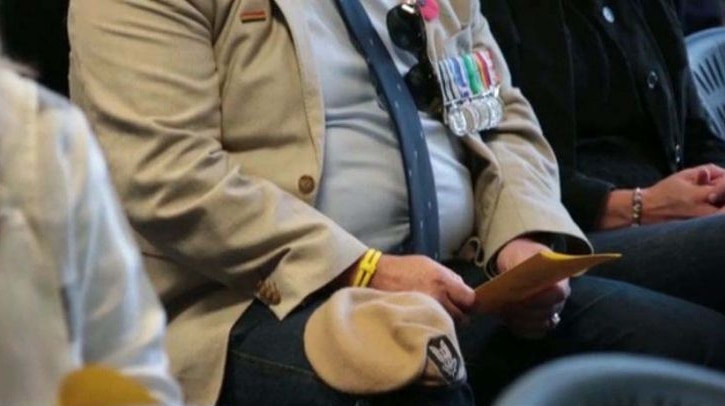 Torso of a man sitting wearing war medals and holding a pamphlet