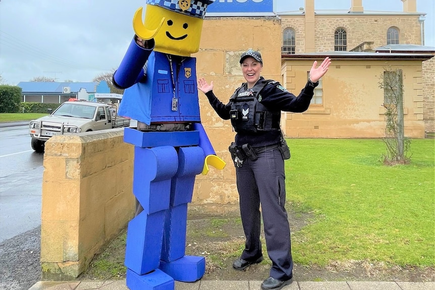 A man wearing a Lego police officer costume with a female police officer outside a police station