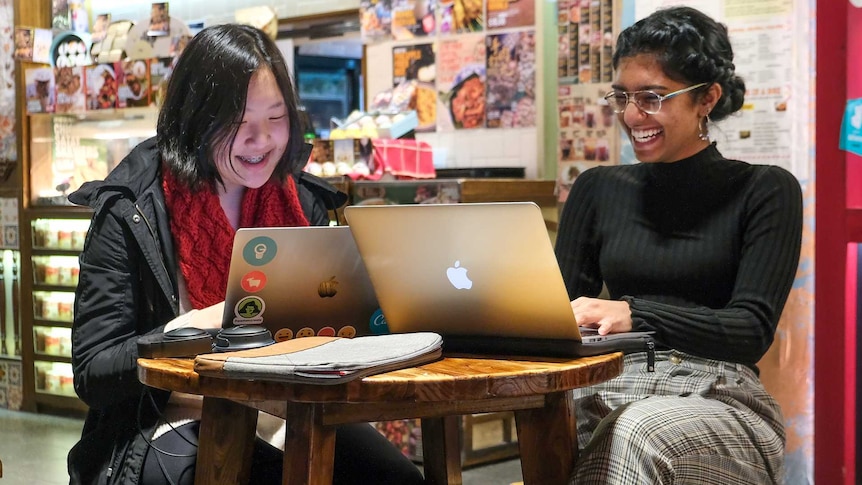 Hannah Ahn and Bagavathy Menon working on their laptops inside a Chatswood food court.