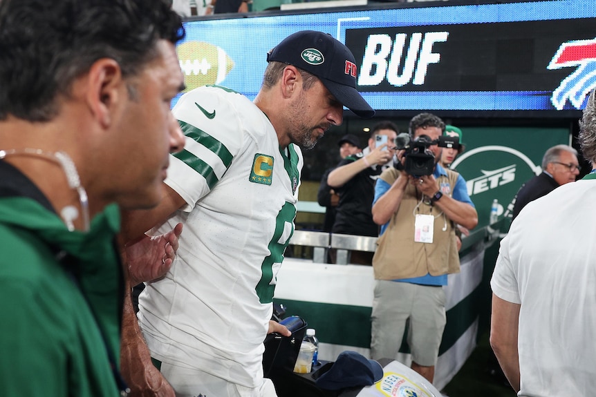 Aaron Rodgers walks off the field with New York Jets trainers after injuring his ankle in their NFL season opener.