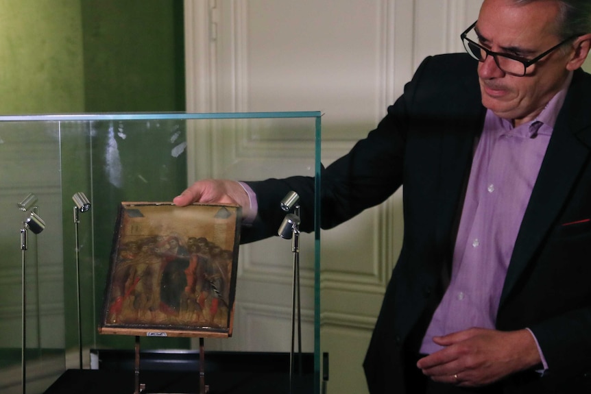 A man carefully takes out a early renaissance painting out of a glass case with lights in it