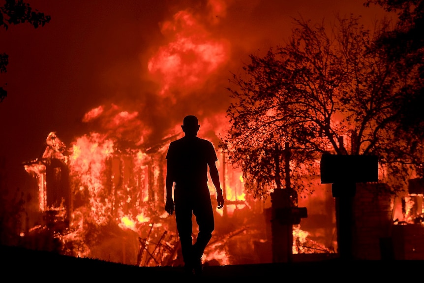 A man is seen in silhouette standing in front of burning homes.