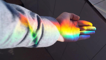 Hand with rainbow light reflecting on it for queer and LGBTIQ support numbers and websites list in Australia
